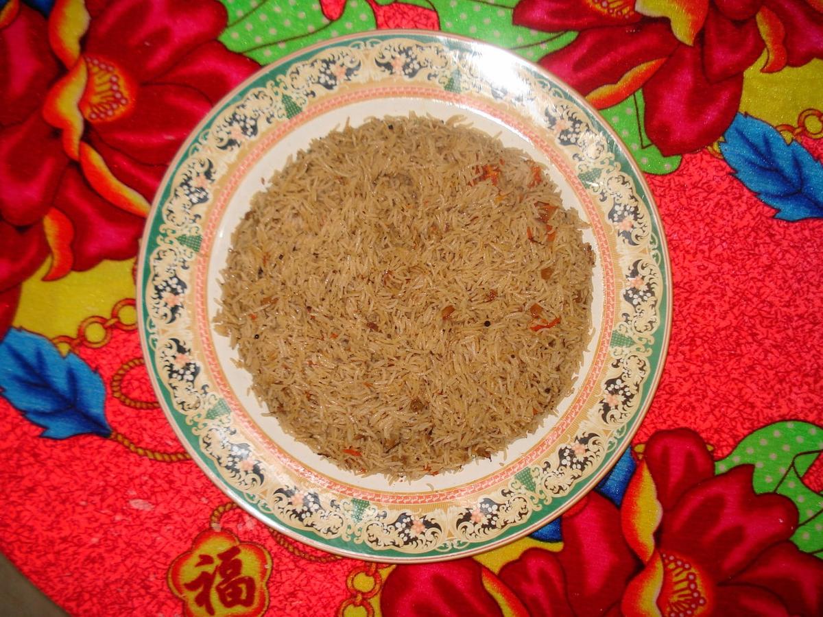 一盤抓飯配胡蘿蔔、葡萄乾、堅果和肉，置於花紋布上。