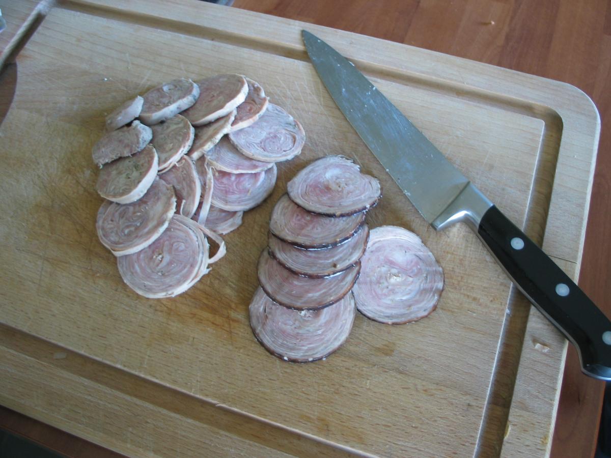 Salsicha pálida fatiada com camadas espirais em uma tábua de corte de madeira.