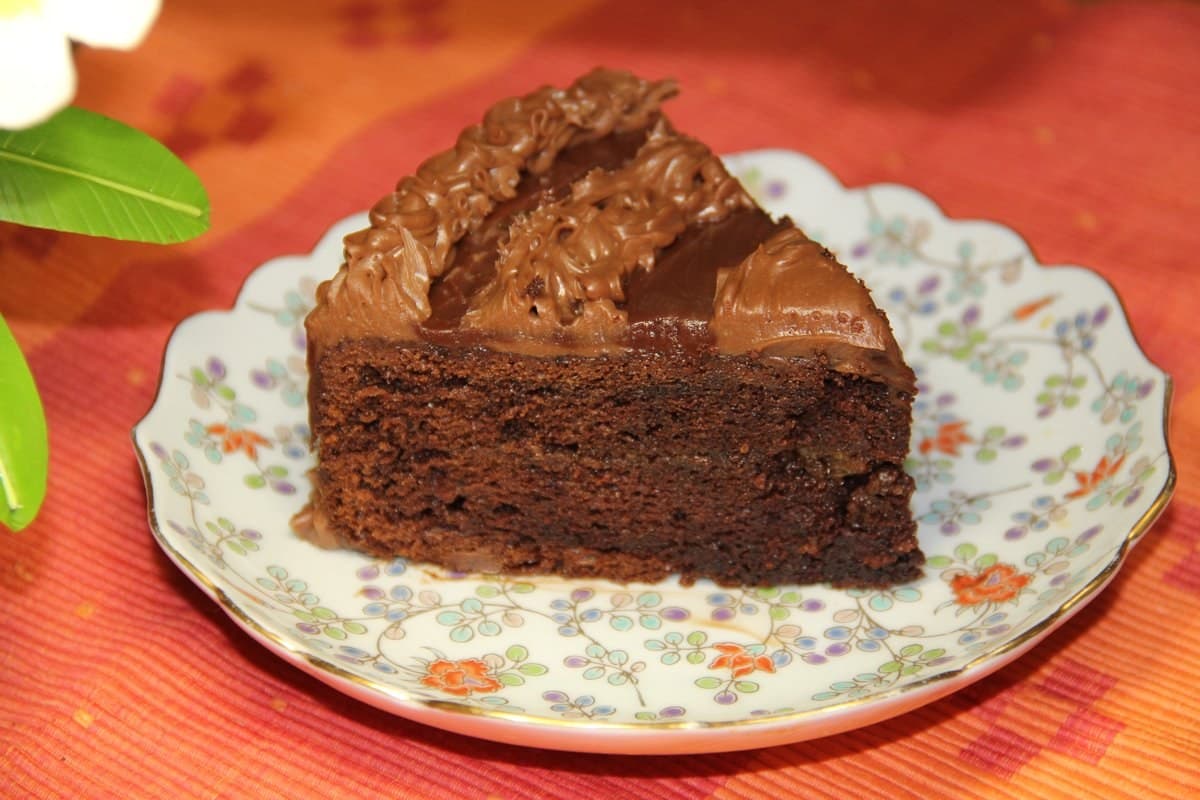 Slice of glossy chocolate cake on a floral plate with a smooth chocolate top.