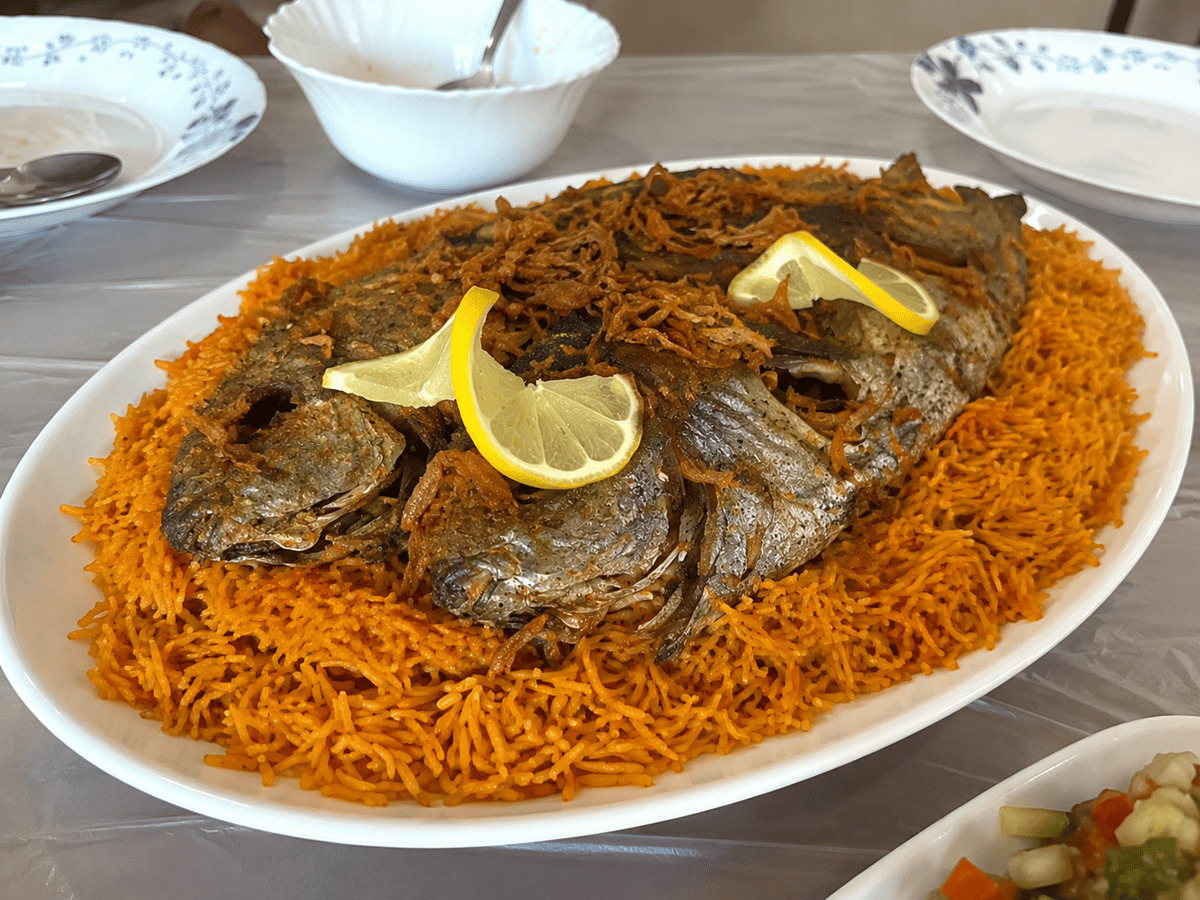 Poisson frit entier avec du citron sur un grand plat de riz orange épicé.