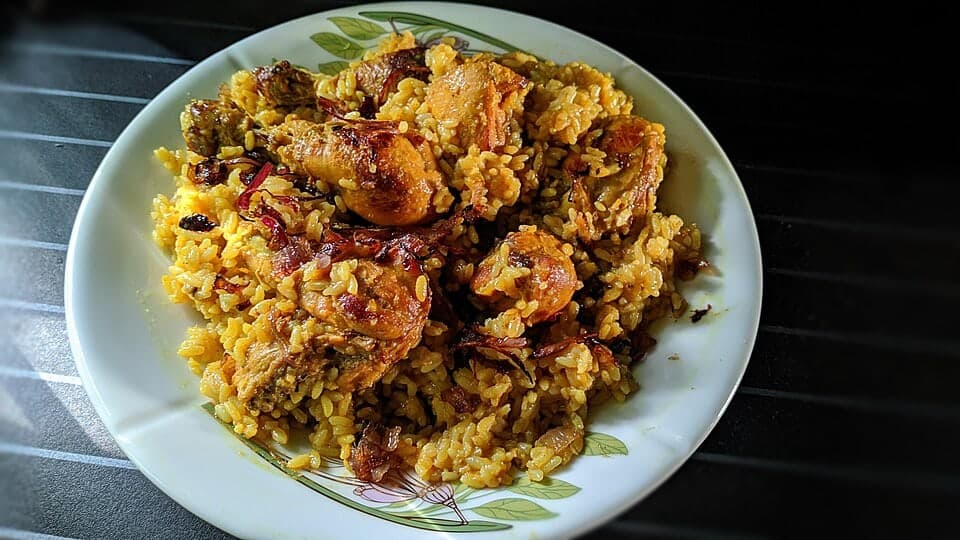 Assiette de polao au poulet avec riz aromatique et morceaux de poulet dorés.