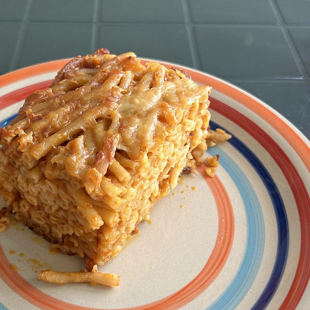 Firm wedge of baked macaroni pie on a striped plate.