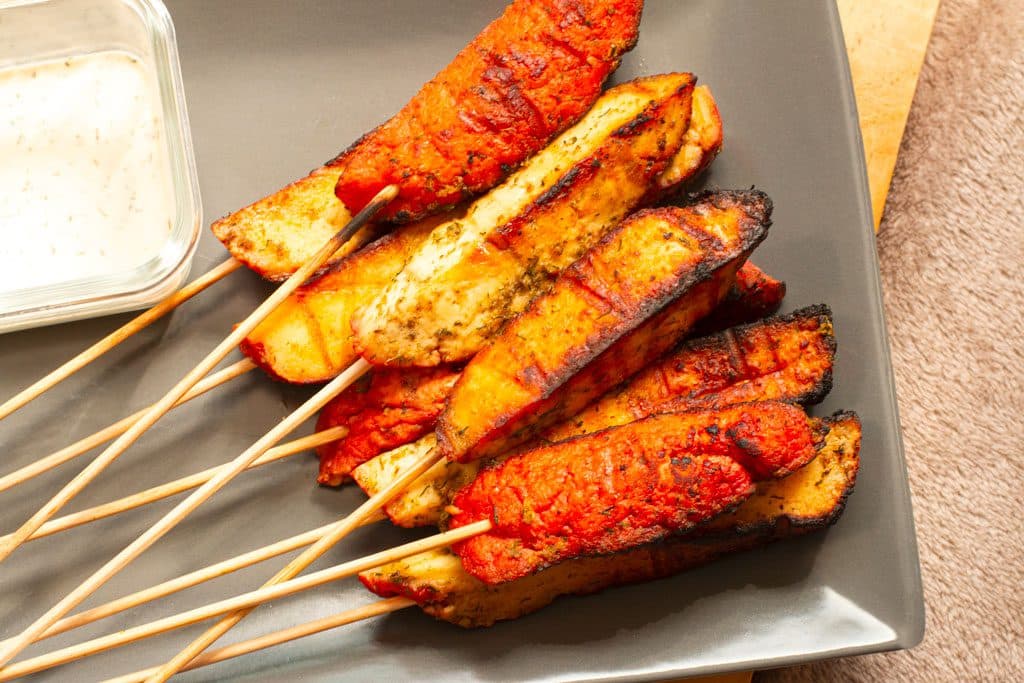 Morceaux de fromage grillé rouge-orange enfilés sur des brochettes en bois à côté d'une petite tasse de sauce à tremper.