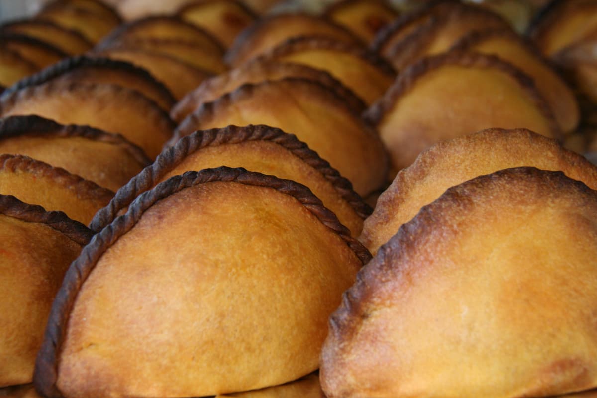 Filas de pasteles dorados horneados en forma de media luna con bordes ondulados oscuros.