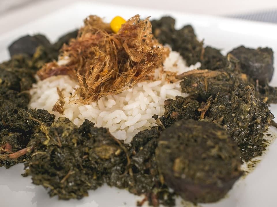Prato com arroz branco cercado por folhas escuras cozidas e pedaços de carne.
