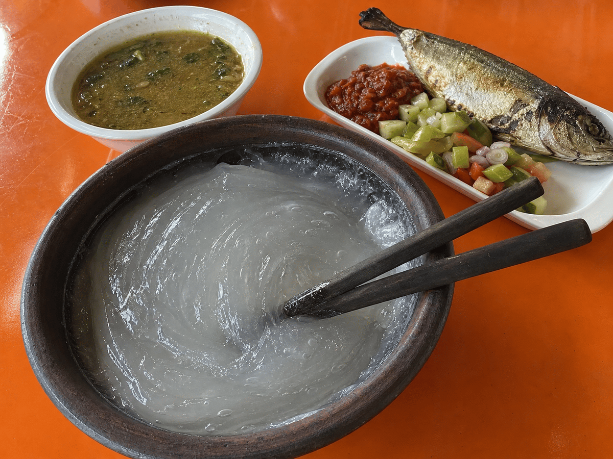 Durchscheinende graue Sagostärke in einer dunklen Schüssel mit hölzernen Chandas, Fisch, Sambal, Gemüse und Soßenbeilagen.