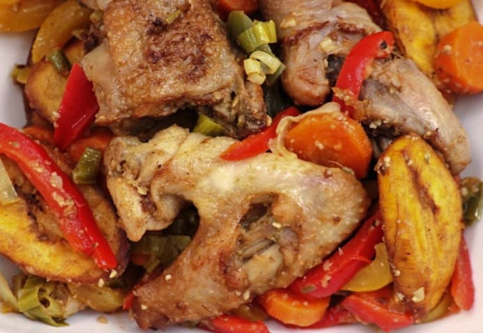 Pedaços de frango com banana frita e legumes em molho brilhante.