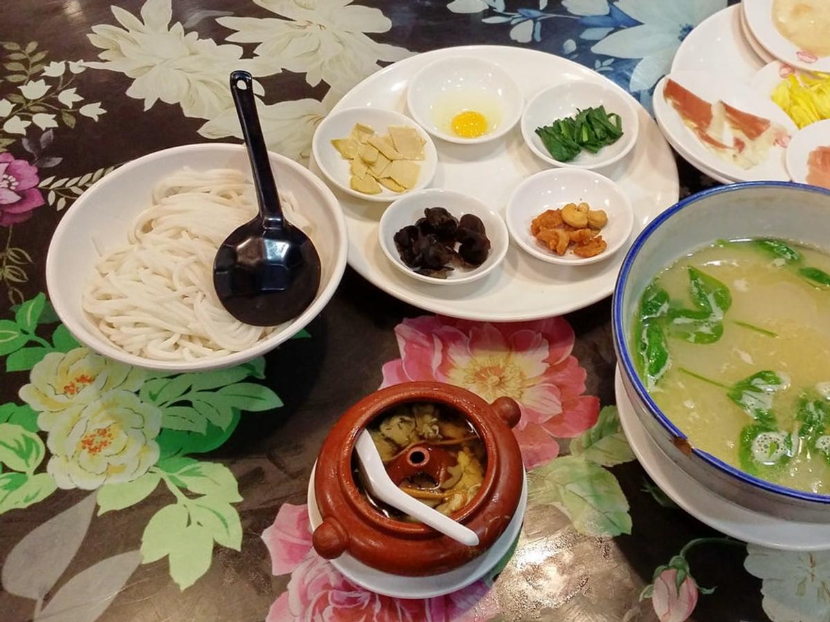Tisch mit Reisnudeln, heißer Brühe und kleinen Tellern mit Zutaten.