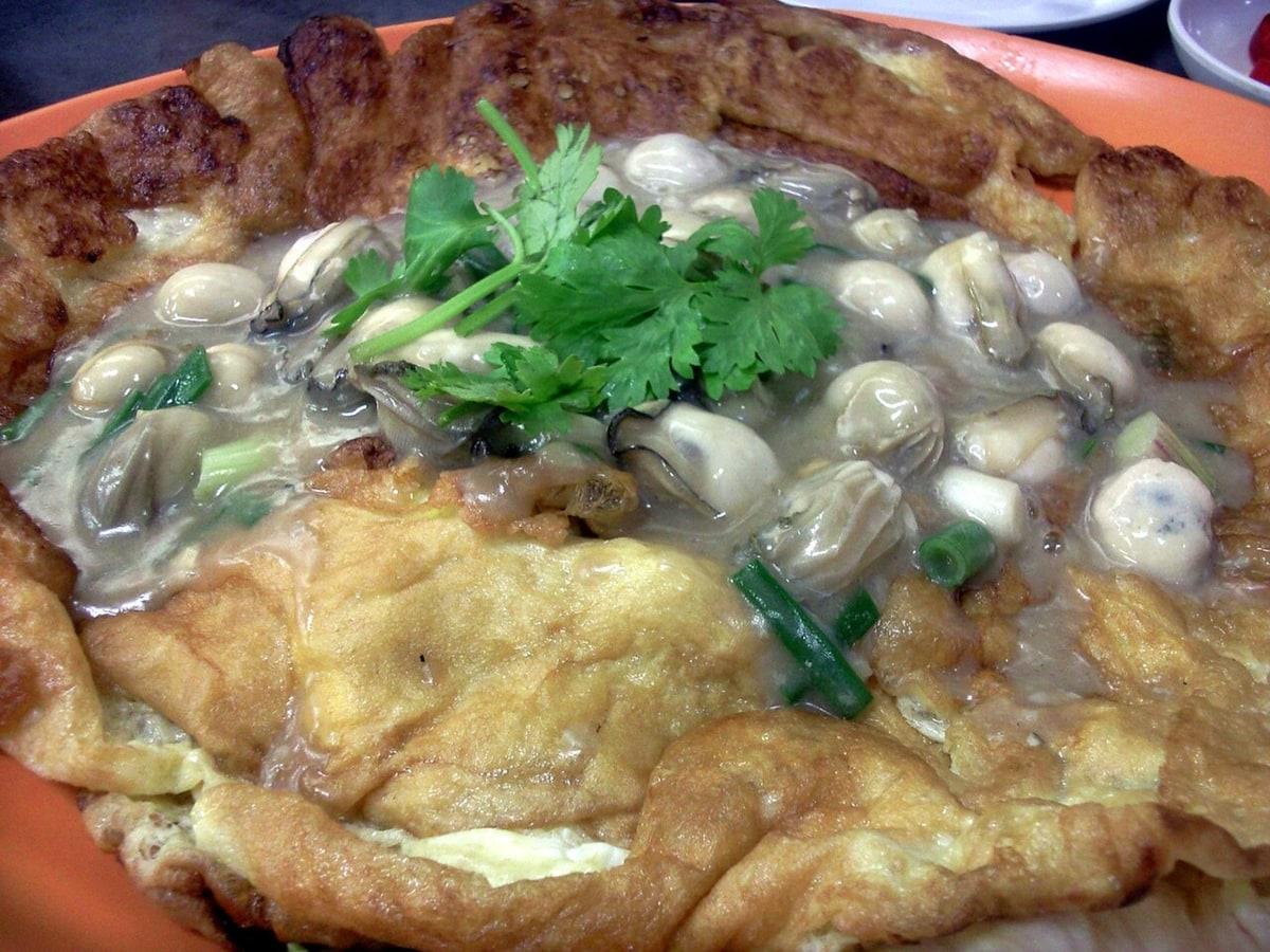 Omelet tiram di piring oranye dengan saus dan rempah.