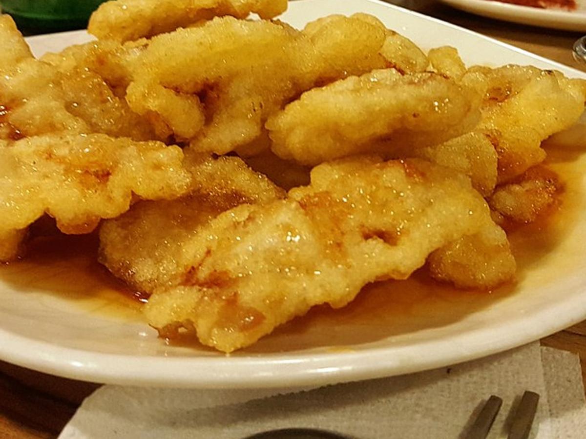 Knusprige Schweinefleischscheiben, überzogen mit glänzender Sauce auf einem weißen Teller.