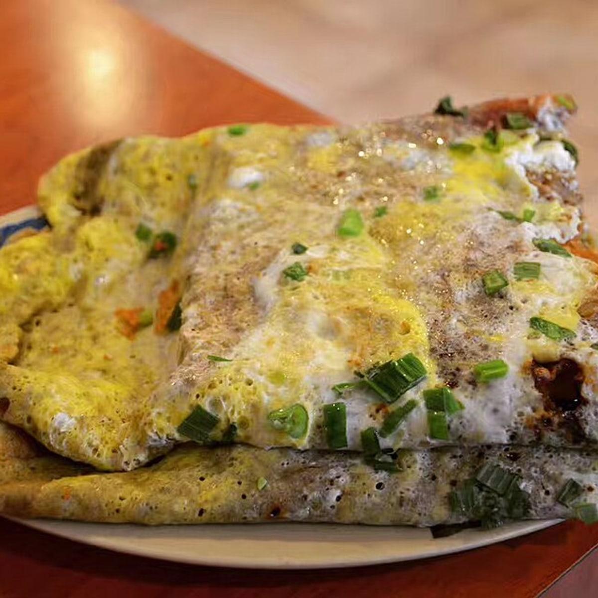 Folded savory crepe with egg, scallions, herbs, sauce, and a crisp insert.