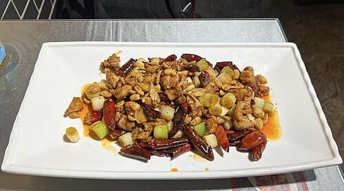 Piring ayam potong dadu yang ditumis dengan kacang tanah, cabai kering, dan daun bawang.