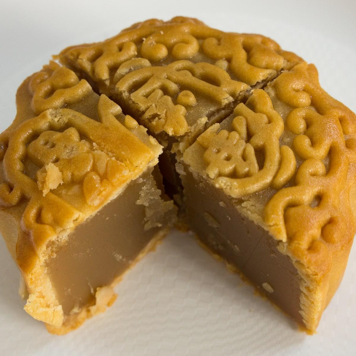 Kue bulan yang dipotong dengan kulit emas yang dicetak dan isian pucat yang padat.