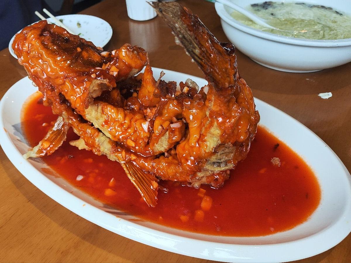 Whole fried carp standing in red sweet-sour sauce on an oval plate.