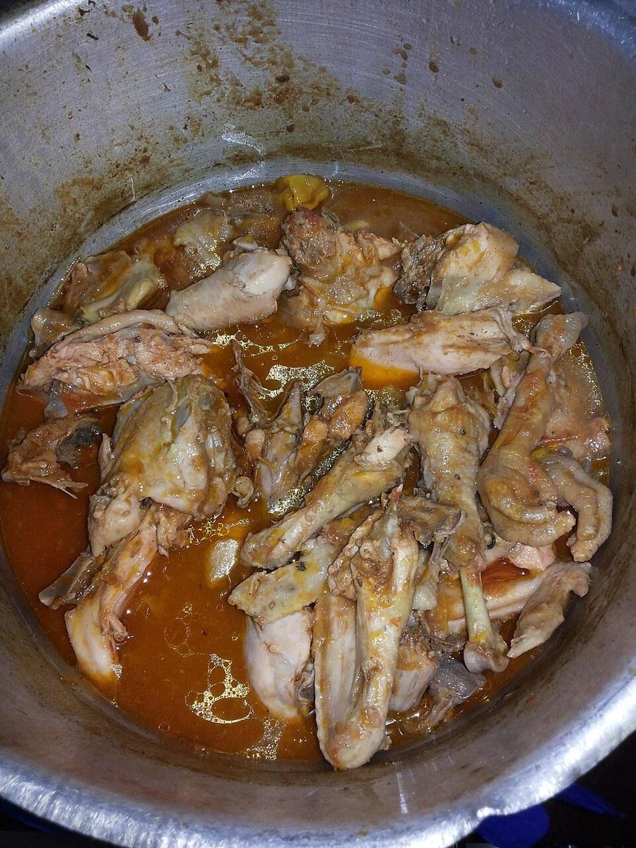 Куски курицы томятся в красноватом рагу внутри металлического горшка.