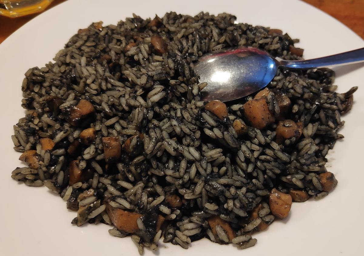 Teller mit schwarzem Meeresfrüchte-Risotto und einem Löffel daneben.
