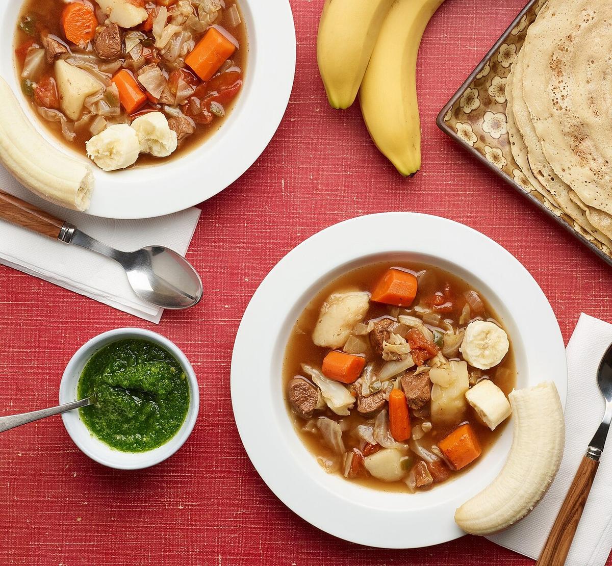 Sopa de carne y verduras con patatas, zanahorias, repollo y tomates, acompañada de plátano y pan plano.