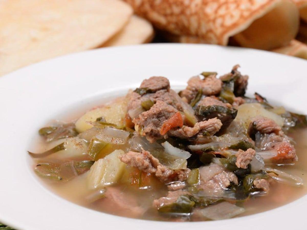 Tigela de sopa de carne clara e vegetais com batata, verduras, tomate e ervas.