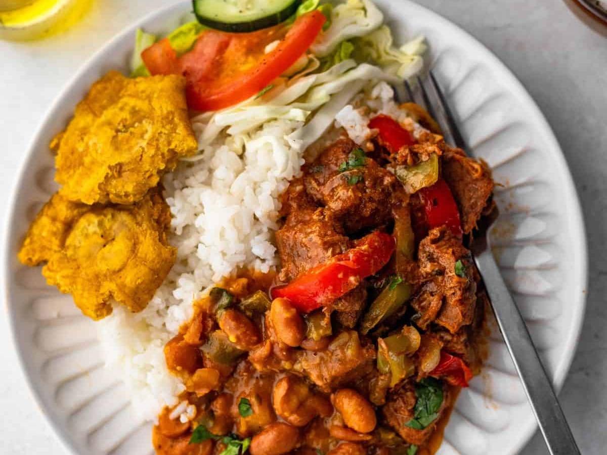 Lunch plate with white rice, stewed beans, stewed meat, plantains, and salad.