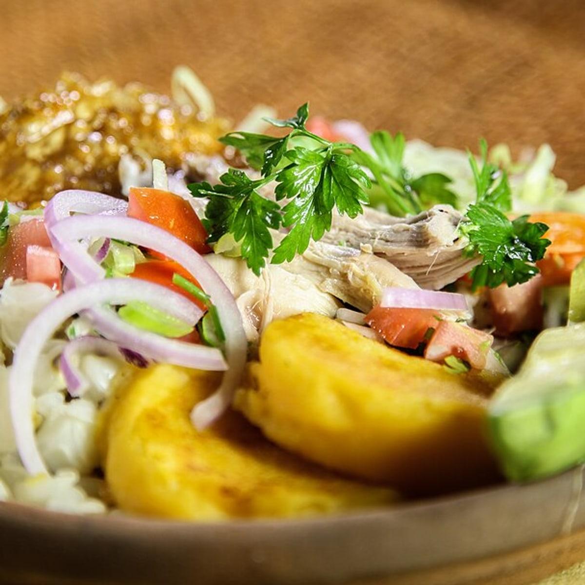 Plate of roast pork with hominy, potato patties, pickled onion, and herbs.