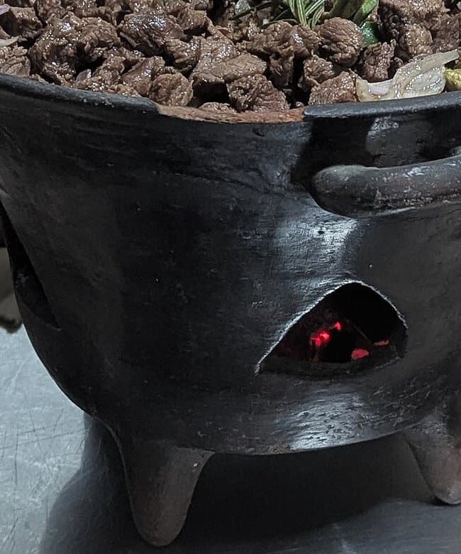 Pfanne mit angebratenen Fleischstücken, die über einer kleinen Flamme sitzen.