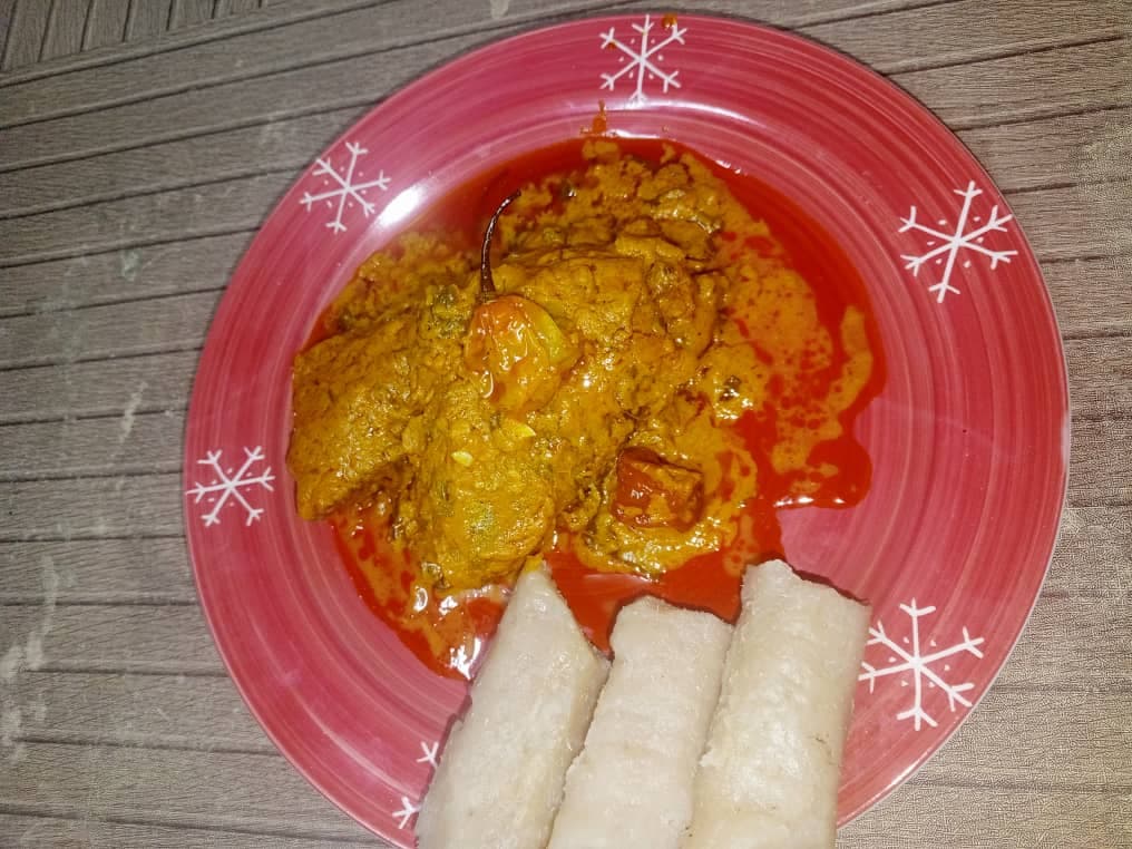 Pollo en salsa de fruta de palma naranja servido con piezas de almidón pálido en un plato.