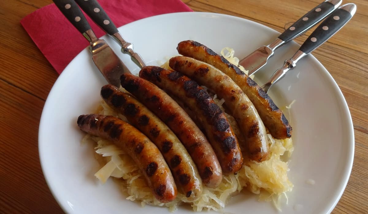Жареные колбаски с квашеной капустой, картофелем и горчицей на тарелке.