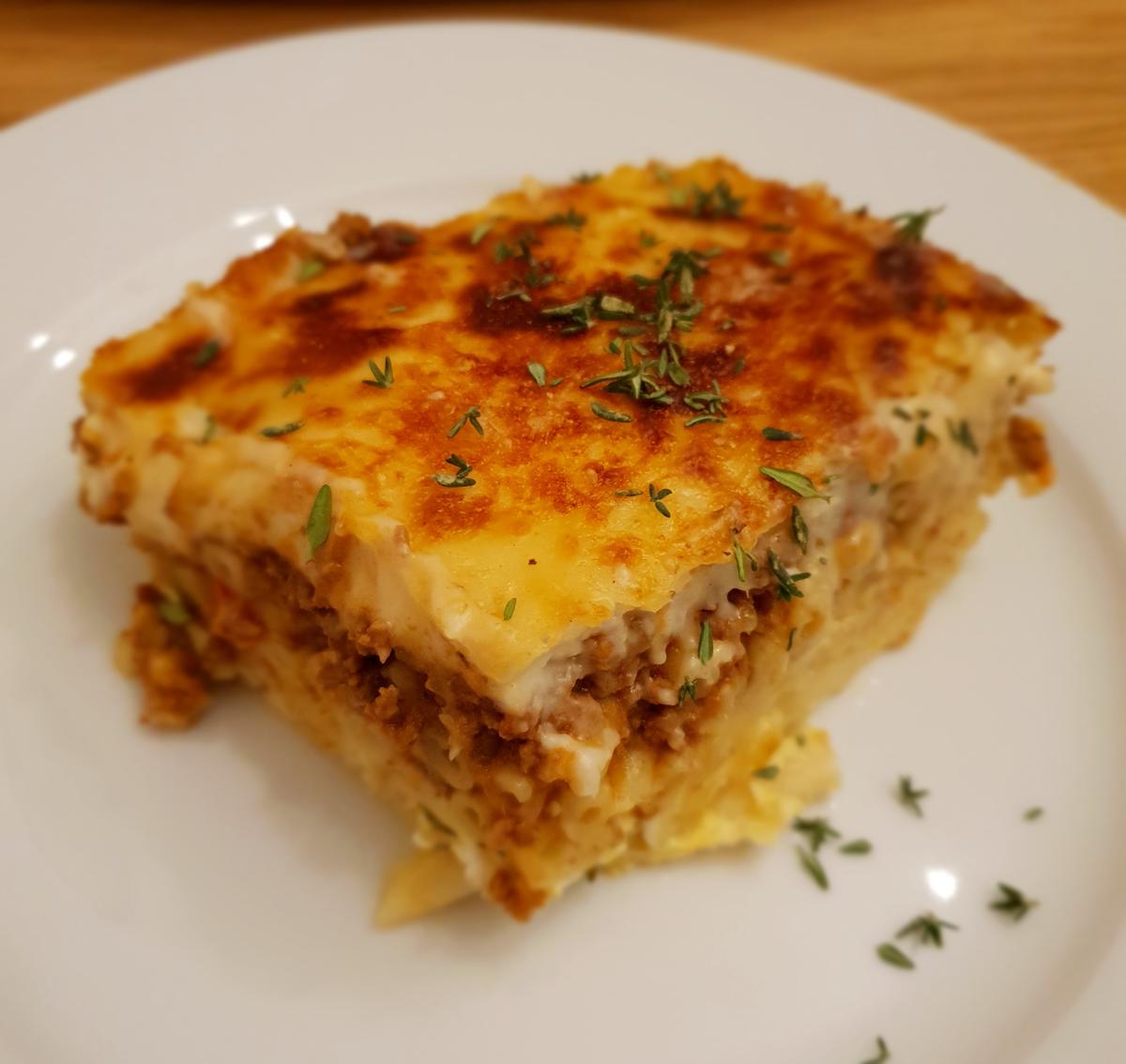 Square slice of baked pasta with meat sauce and a creamy golden top on a white plate.