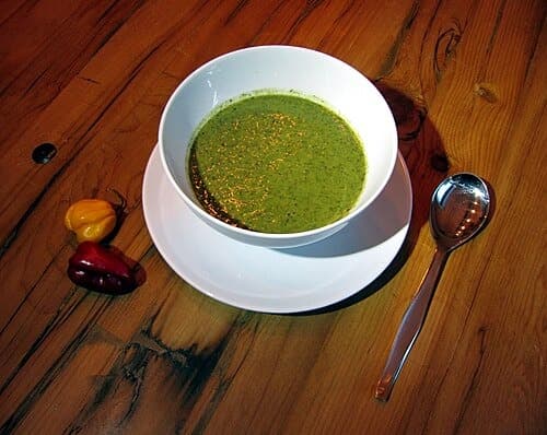 Schüssel mit dicker grüner Blattgemüsesuppe und Löffel auf einem Holztisch.