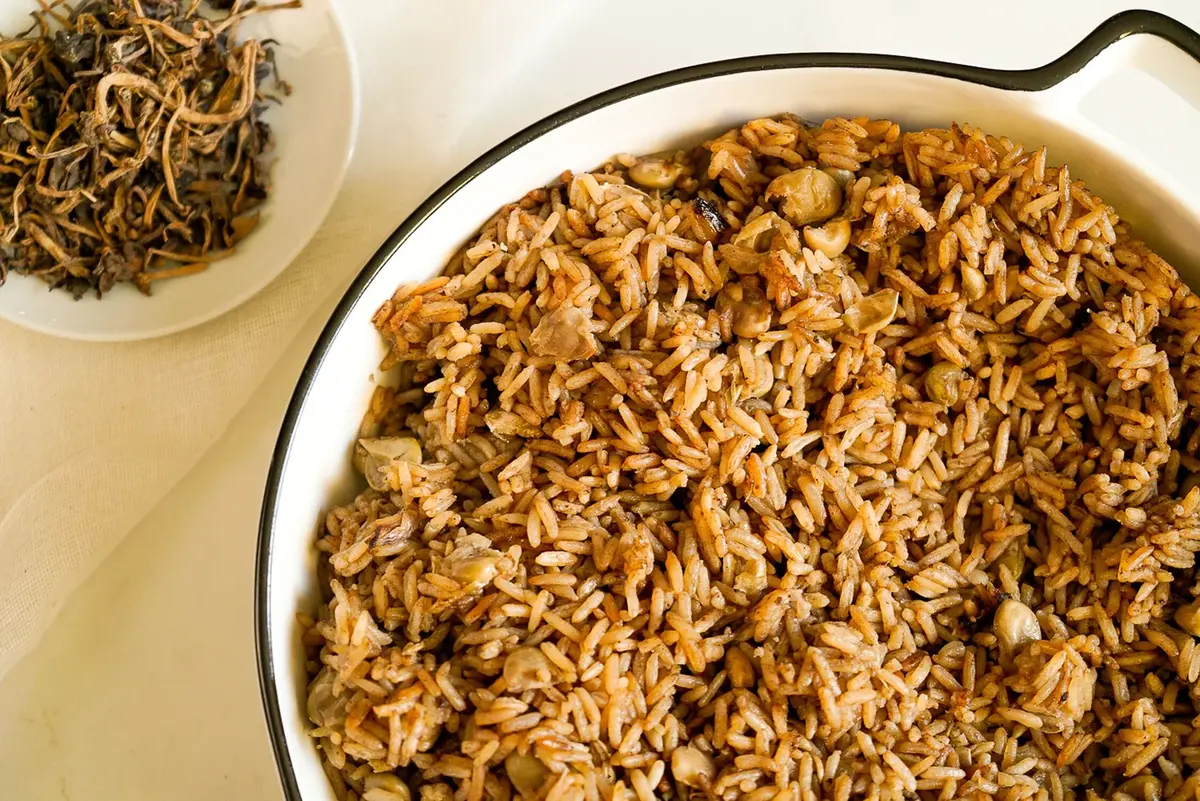 Plato poco profundo de arroz de champiñones oscuros con granos visibles y un pequeño plato de champiñones secos cerca.