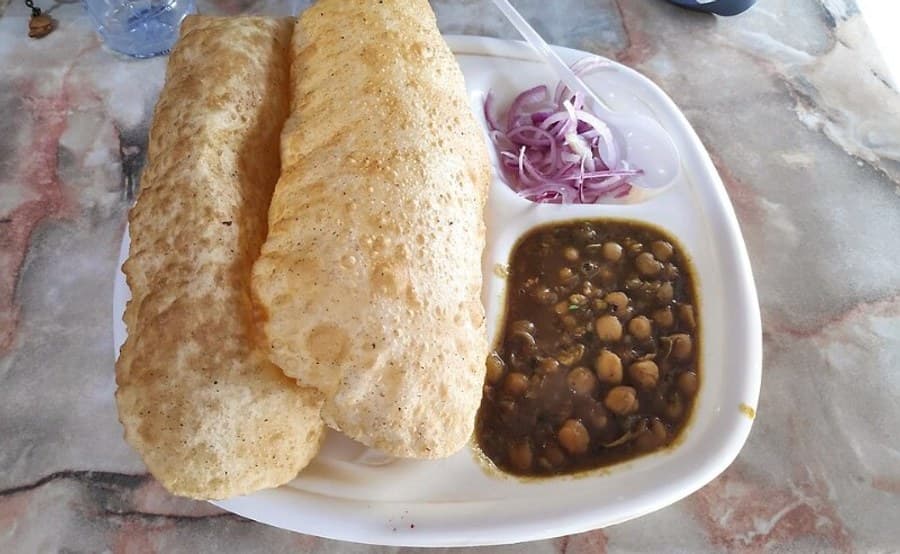 Two puffed fried breads served with chickpea curry and sliced onion on a white plate.