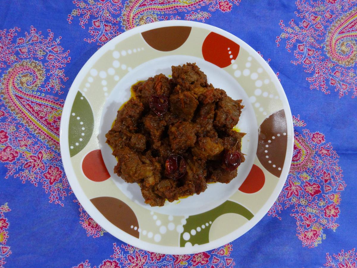 Темные куски говядины в густой пряной кокосовой пасте рядом с рисом.