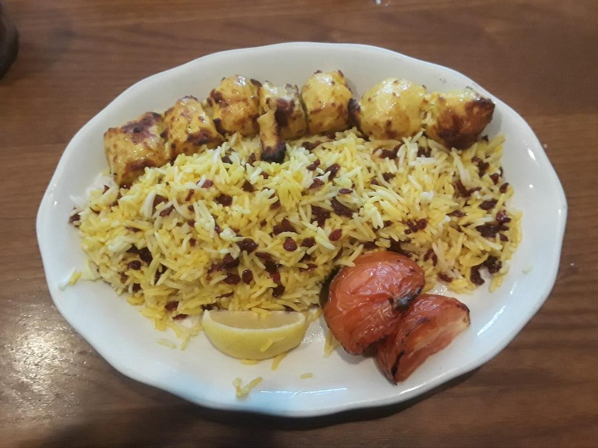 Barberry-speckled saffron rice served with pieces of chicken on a white plate.