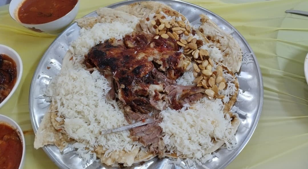 Gebratene Lammfleischstücke auf weißem Reis mit Mandeln und kleinen Schüsseln mit Soße.