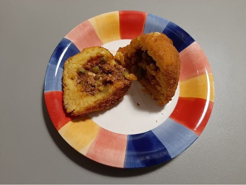 Geteiltes frittierte Reisbällchen, das eine Fleischsauce-Füllung auf einem Teller zeigt.