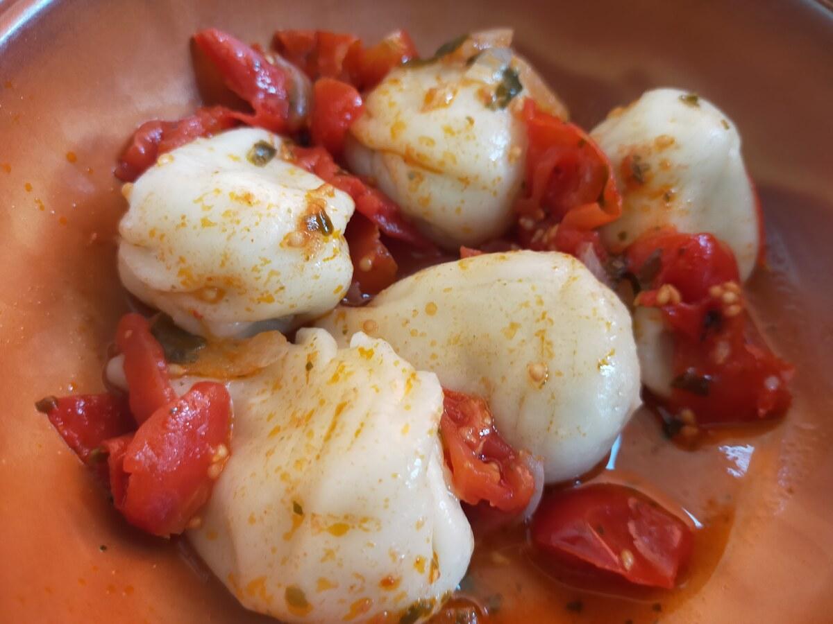 Raviolis blancs plissés avec morceaux de tomate sur une assiette simple.