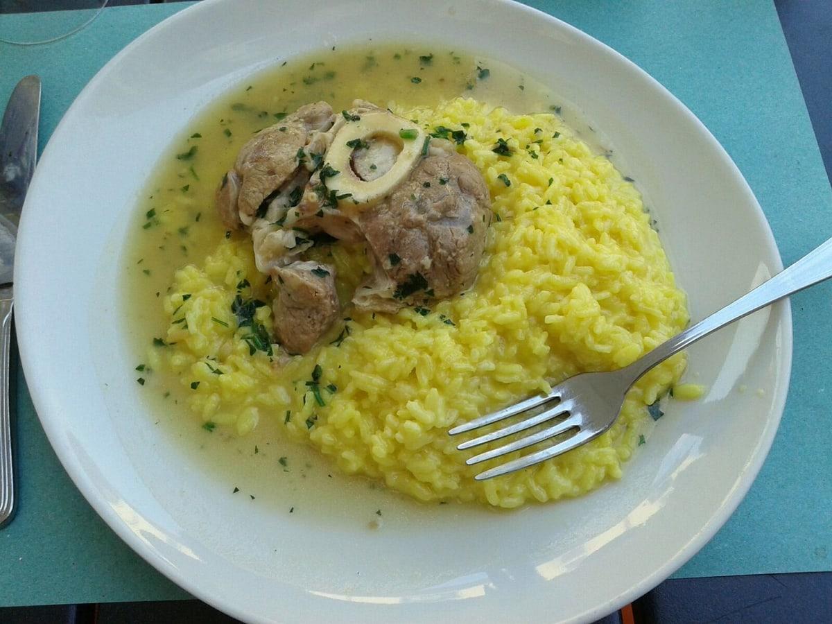 Geschmorte Kalbshaxe mit sichtbarem Markknochen, serviert mit gelbem Risotto.