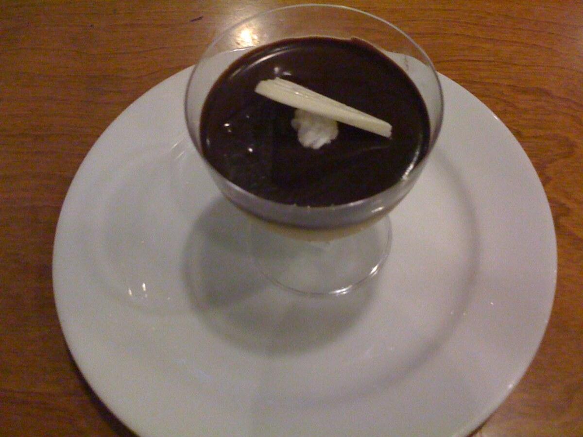 Segelas kecil makanan penutup krim dengan taburan saus hitam di atas piring putih.