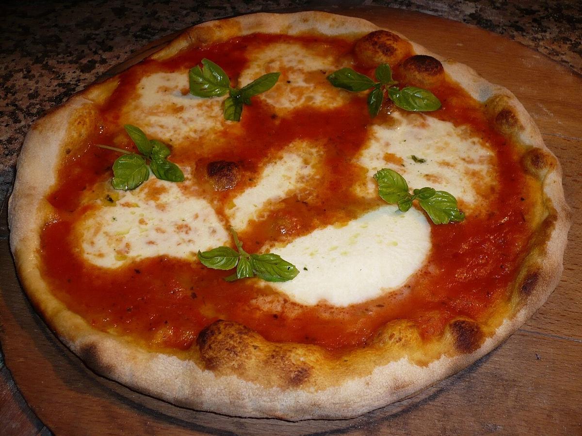 Pizza bundar dengan topping saus tomat, mozzarella, dan daun kemangi.