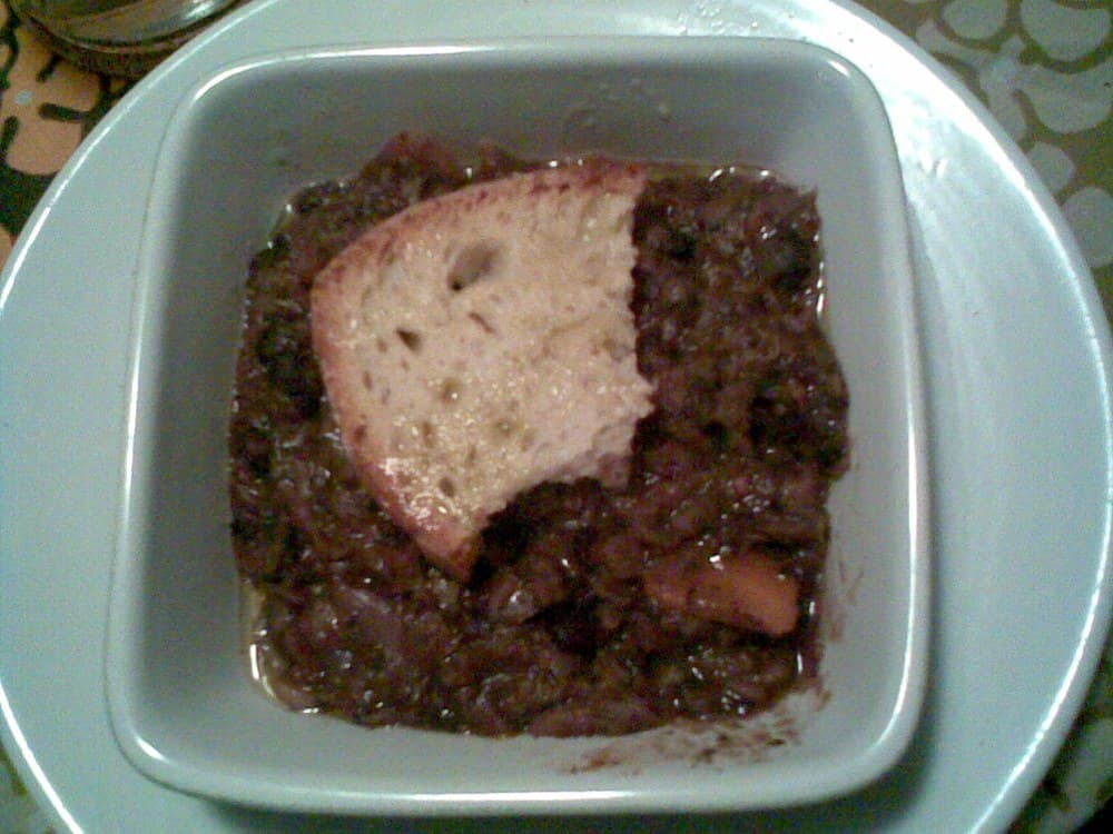 Sup sayuran dan kacang kental yang gelap ditambahkan dengan sepotong roti di mangkuk persegi.