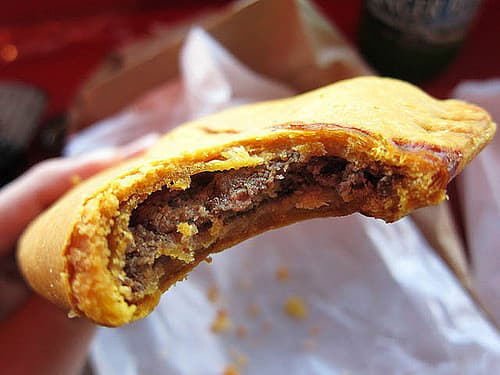 Empanada de carne de res hojaldrada de color amarillo con un bocado que revela un relleno picado oscuro.