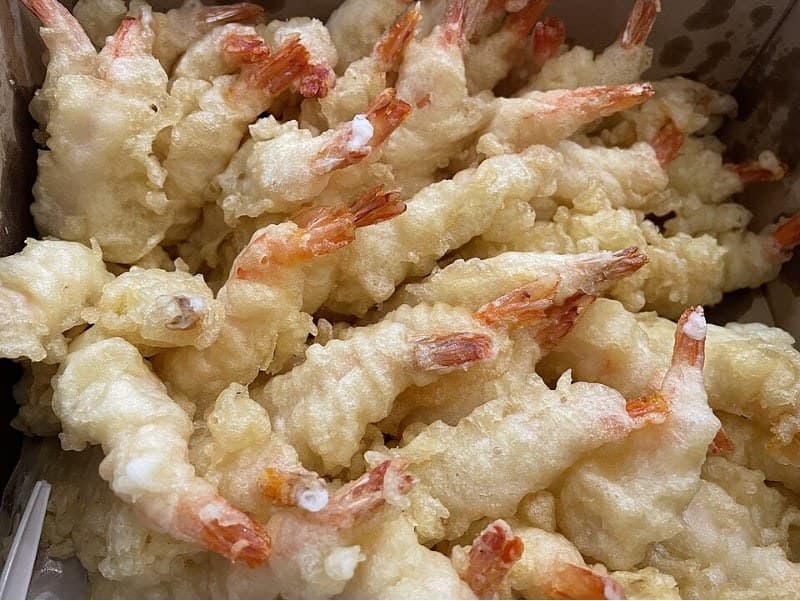 Potongan udang tempura yang dilapisi adonan ditumpuk di atas nampan.