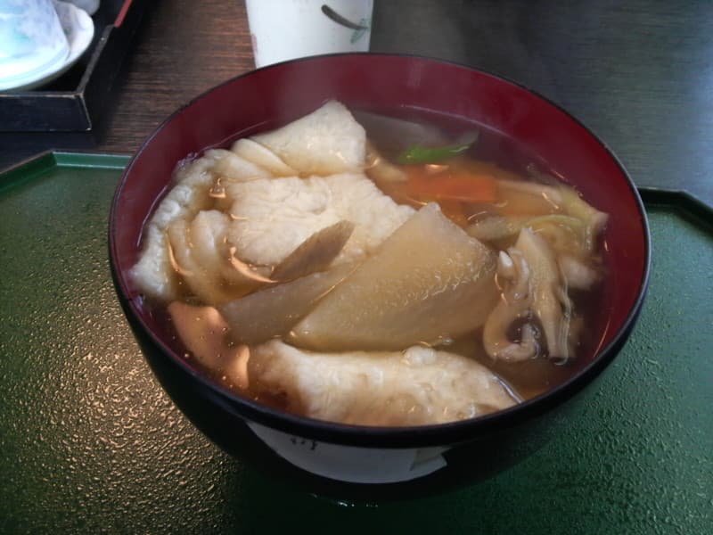 Eine rote Schüssel Suppe mit weichen Weizenkeksen, Gemüse und Brühe.