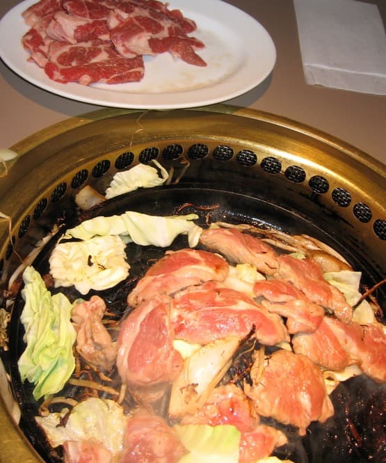 Lamm- und Gemüsestücke, die auf einem runden Tischgrill garen.
