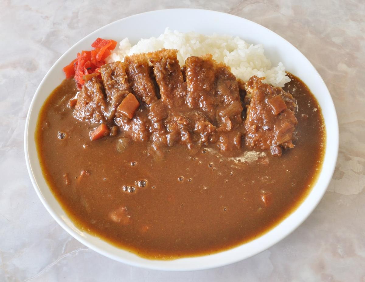 Geschnittenes, paniertes Schnitzel mit brauner Currysauce und weißem Reis auf einem Teller.