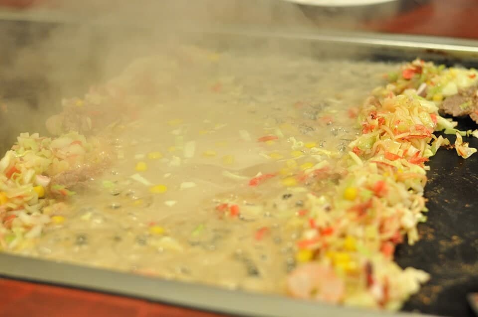 Flüssiger herzhafter Teig mit gehackten Toppings, die auf einer dampfenden Platte kochen.