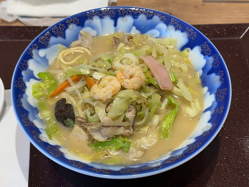 Eine Schüssel mit trüber Nudelsuppe, Garnelen, Schweinefleisch, Kohl, Sojasprossen und Fischkuchen.