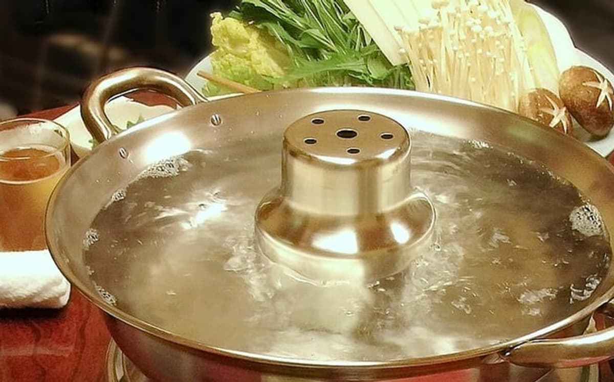 冒泡的桌上火锅，后面摆着蔬菜。