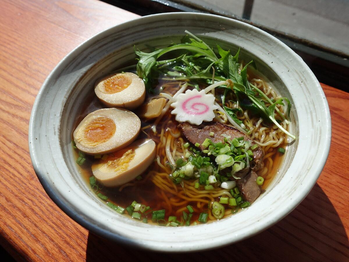 Semangkuk ramen berbumbu kedelai dengan mie, chashu, daun bawang, dan telur.