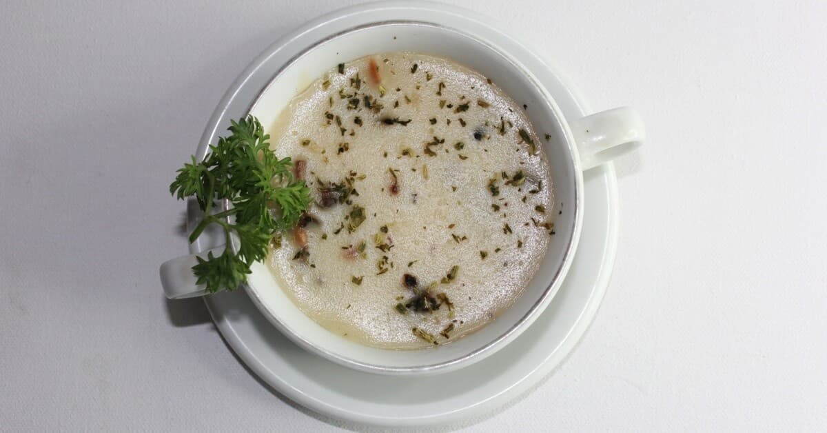 White cup of creamy soup flecked with herbs and spices on a saucer.